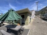 Exterior of Sunrise Juice in Bingen, WA with a green patio umbrella, picnic table, green bistro chairs and an open door under blue sky